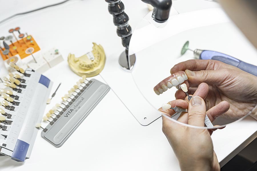 Dental technician selecting denture teeth shade and customizing same day dentures in Midtown NYC dental lab